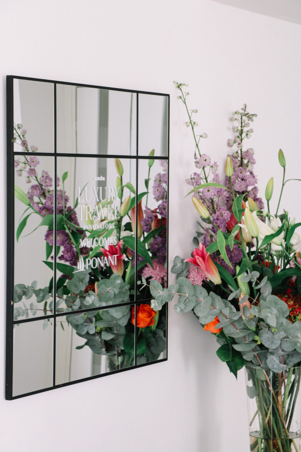 A logo on a mirror that says Luxury Travel Innovators Welcomes Ponant, with a gorgeous flower arrangement in front